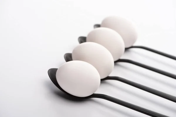 Selective focus of white chicken eggs on black spoons on white surface — Stock Photo