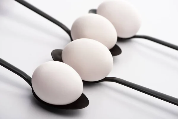 Selective focus of chicken eggs on black spoons on white surface — Stock Photo