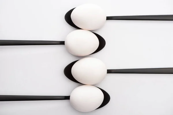 Top view of white chicken eggs on black spoons on white background — Stock Photo