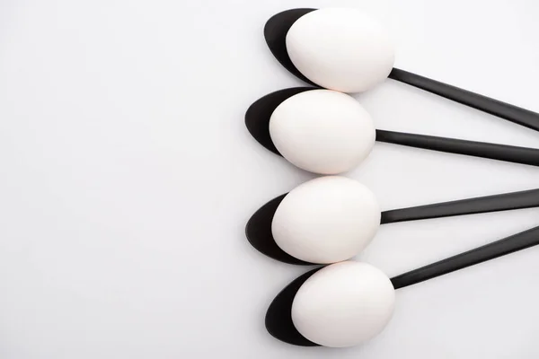 Top view of chicken eggs on black spoons on white surface — Stock Photo