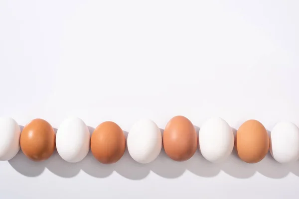 Vue de dessus des œufs de poulet blancs et bruns sur la surface blanche — Photo de stock