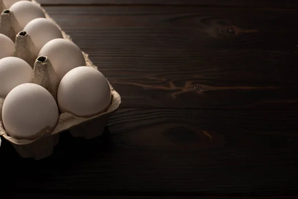 Chicken eggs in egg tray on dark wooden surface — Stock Photo