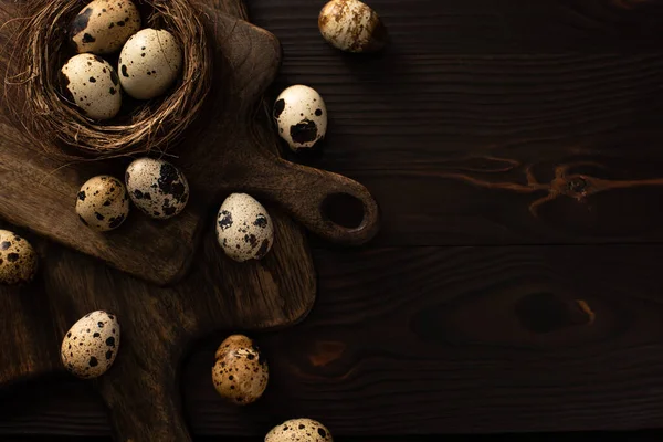 Top view of quail eggs in nest and on brown cutting boards on dark wooden surface — Stock Photo