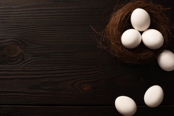 Vue du dessus des œufs de poule blancs dans le nid et sur fond de bois brun — Photo de stock