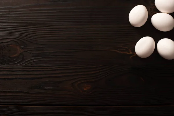 Верхний вид белых куриных яиц на темном деревянном фоне — стоковое фото