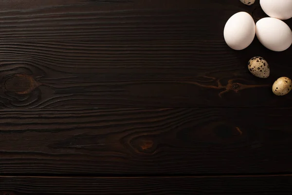 Vista dall'alto di uova di pollo bianche e uova di quaglia su una superficie di legno marrone — Foto stock