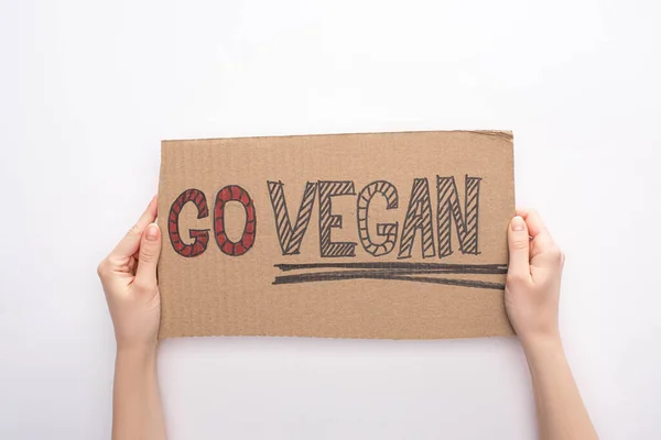 Vista parziale della donna che tiene segno di cartone con iscrizione vegana go su sfondo bianco — Foto stock