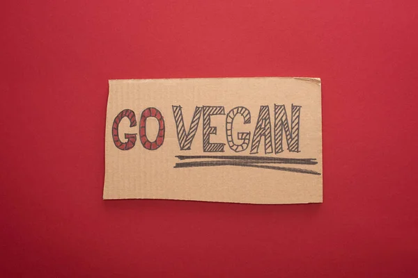 Vista superior del cartel de cartón con inscripción vegana go sobre fondo rojo - foto de stock