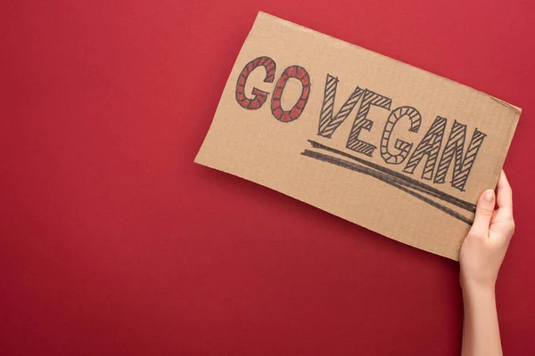 Partial view of woman holding sign with go vegan inscription on red background — Stock Photo