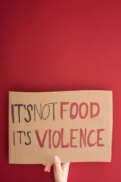 Partial view of woman holding cardboard sign with its not food its violence inscription on red background — Stock Photo