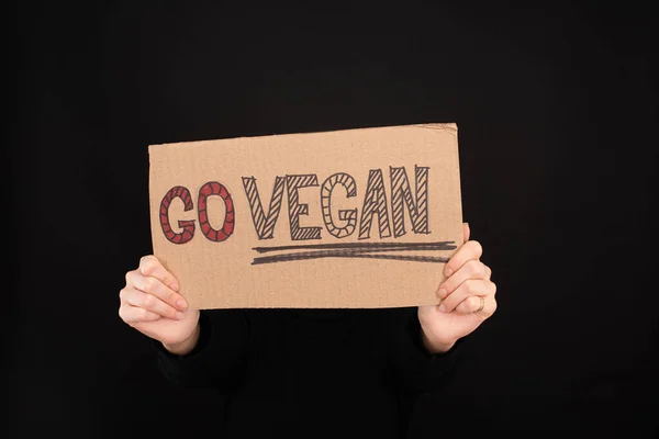 Partial view of woman holding sign with go vegan inscription isolated on black — Stock Photo