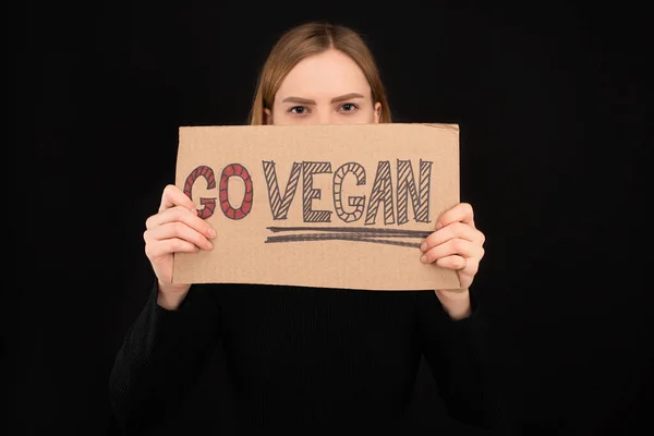 Mulher com rosto obscuro segurando papelão com go inscrição vegan isolado em preto — Fotografia de Stock