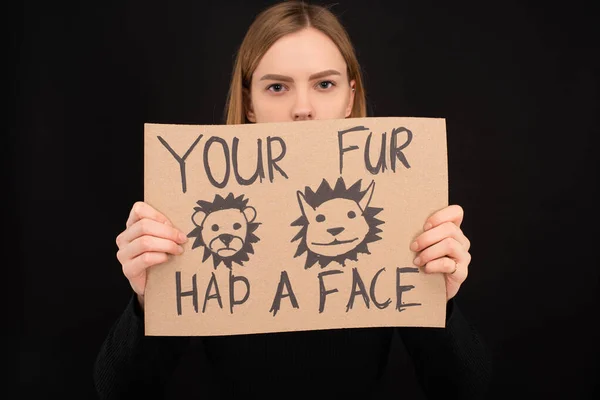 Woman with obscure face holding cardboard sign with your fur had a face inscription isolated on black — Stock Photo