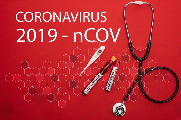 Vue du dessus du stéthoscope, du thermomètre et des éprouvettes avec échantillons de sang et inscription du coronavirus 2019-ncov sur fond rouge — Photo de stock