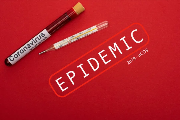 Top view of test tube with blood sample and thermometer with epidemic coronavirus illustration on red background — Stock Photo