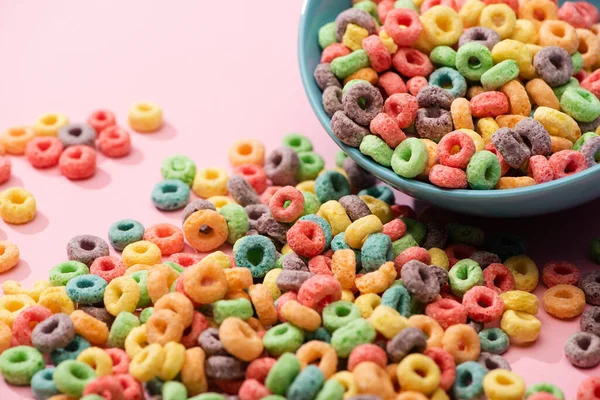 Bright colorful breakfast cereal scattered from bowl on pink background — Stock Photo