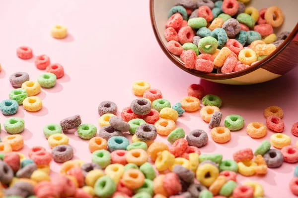 Selective focus of bright colorful breakfast cereal scattered from bowl on pink background — Stock Photo