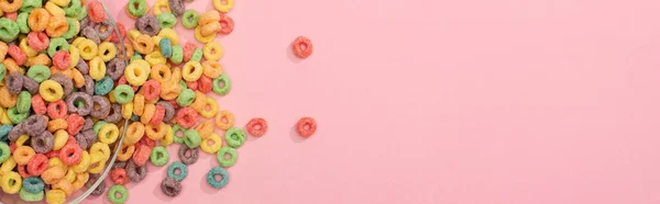 Top view of bright colorful breakfast cereal scattered from bowl on pink background, panoramic shot — Stock Photo