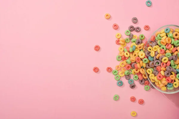 Top view of bright colorful breakfast cereal scattered from bowl on pink background — Stock Photo