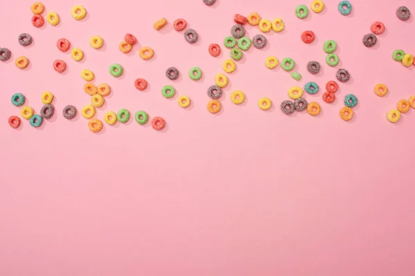 Vista superior de cereales de desayuno multicolores brillantes dispersos sobre fondo rosa - foto de stock