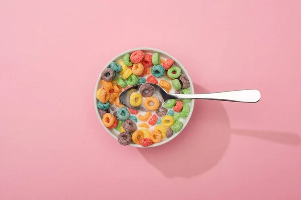 Vista superior de los cereales de desayuno de colores brillantes en tazón con cuchara sobre fondo rosa - foto de stock