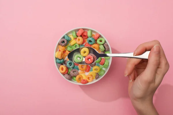 Partial view of woman eating bright colorful breakfast cereal from bowl with spoon on pink background — Stock Photo