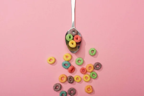 Vista superior de los cereales de desayuno de colores brillantes dispersos de cuchara sobre fondo rosa - foto de stock