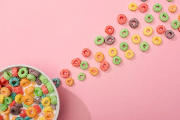 Vista superior de los cereales de desayuno de colores brillantes con leche en el tazón y alrededor sobre fondo rosa - foto de stock