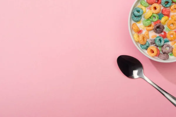 Draufsicht auf helle bunte Frühstückscerealien mit Milch in Schüssel in der Nähe von Löffel auf rosa Hintergrund — Stockfoto