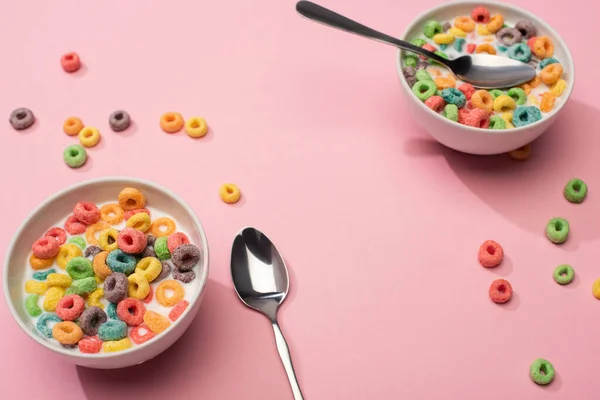 Foco seletivo de cereal de café da manhã colorido brilhante com leite em tigelas com colheres no fundo rosa — Fotografia de Stock