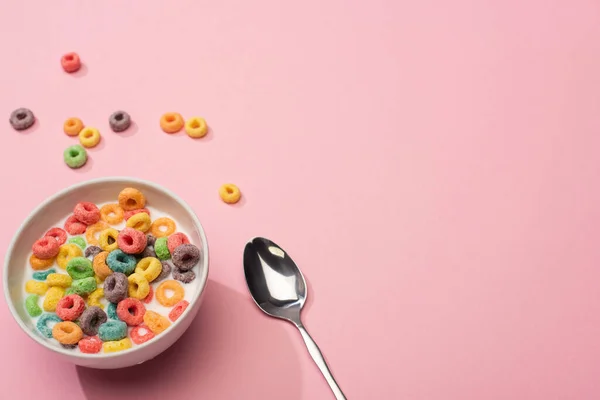 Helle bunte Frühstückszerealien mit Milch in Schüssel mit Löffel auf rosa Hintergrund — Stockfoto