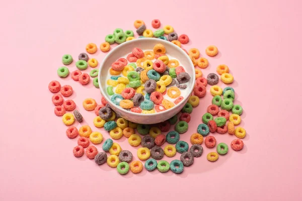 Bright colorful breakfast cereal with milk in bowl and around on pink background — Stock Photo