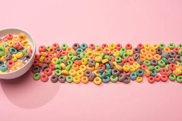 Cereales coloridos brillantes para el desayuno con leche en tazón y sobre fondo rosa - foto de stock