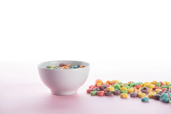 Bright multicolored breakfast cereal scattered around bowl on white background — Stock Photo