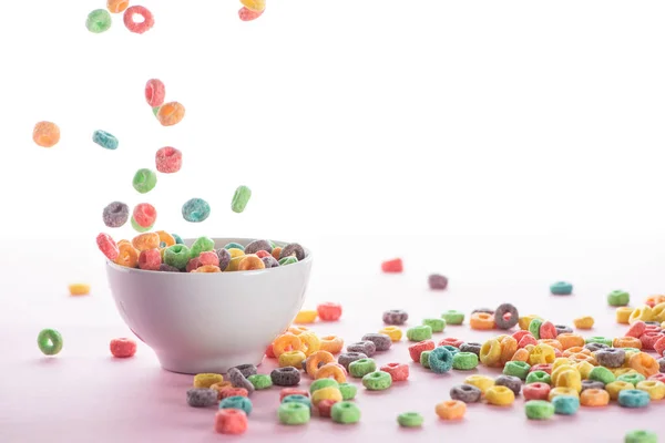 Brillante cereal de desayuno multicolor cayendo en un tazón sobre fondo blanco - foto de stock