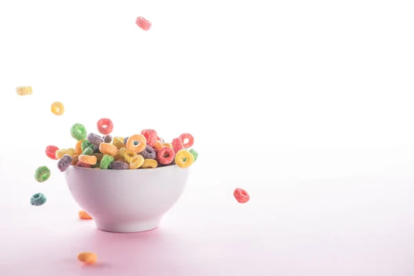 Bright multicolored breakfast cereal falling in bowl on white background — Stock Photo