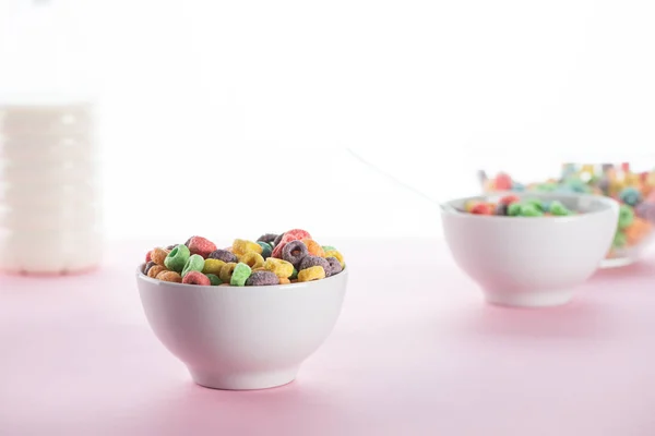 Foco seletivo de cereal de café da manhã multicolorido brilhante em tigelas perto de leite no fundo branco — Fotografia de Stock