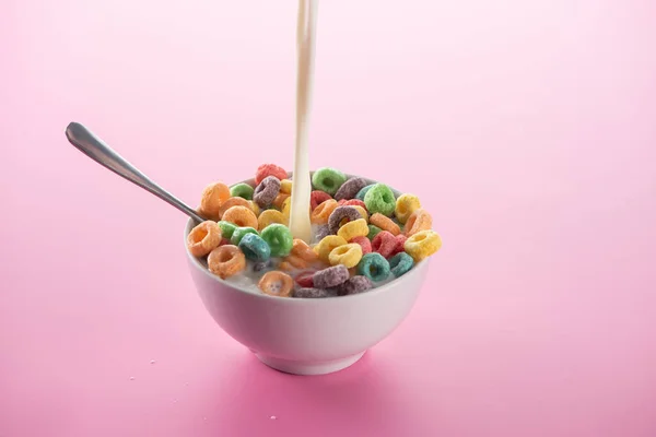 Яскравий різнокольоровий сніданок каші в мисці з заливкою молока і ложки на рожевому фоні — стокове фото