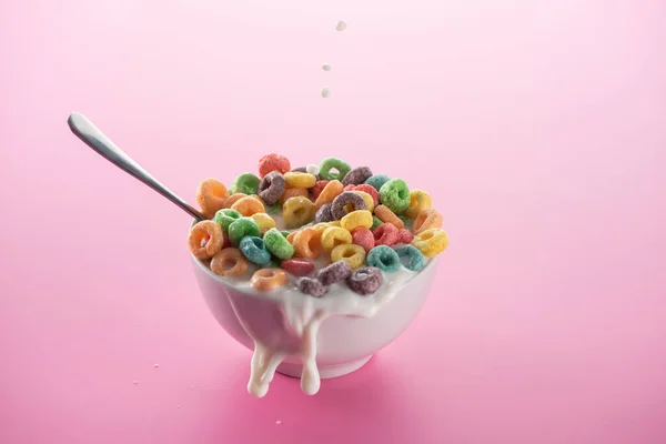 Bright multicolored breakfast cereal in bowl with splashing milk and spoon on pink background — Stock Photo