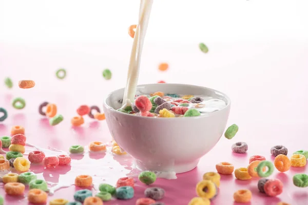 Brilhante cereal café da manhã multicolorido em tigela com derramamento de leite no fundo rosa — Fotografia de Stock