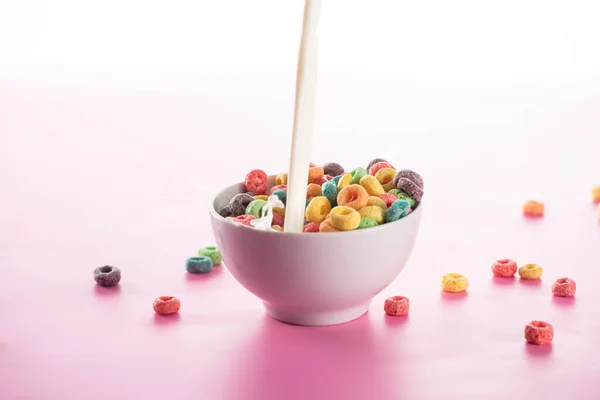 Bright multicolored breakfast cereal in bowl with pouring milk on pink background — Stock Photo