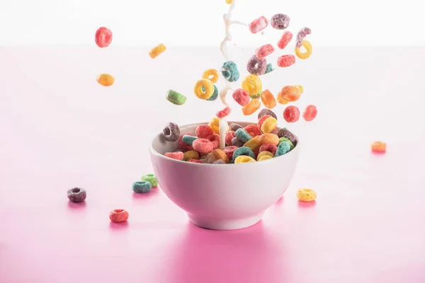 Bright multicolored breakfast cereal in bowl with milk splash on pink background — Stock Photo