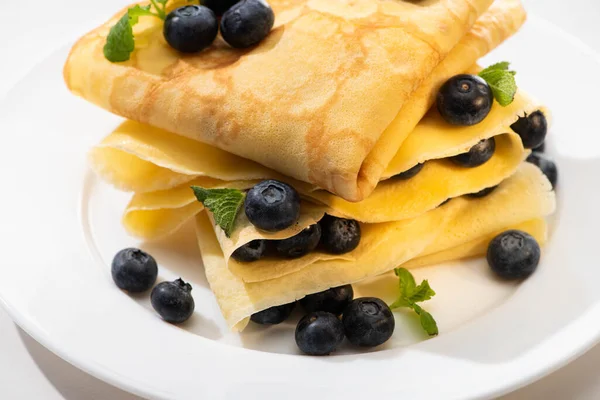 Vista de cerca de crepes sabrosos con menta y arándanos en el plato sobre fondo blanco - foto de stock