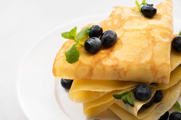 Close up view of tasty crepes with mint and blueberries on plate on white background — Stock Photo