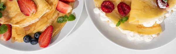 Вид сверху на вкусные блины с ягодами на тарелках на белом фоне, панорамный снимок — стоковое фото