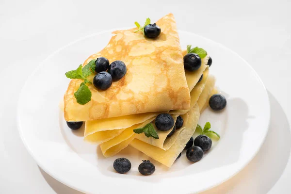 Tasty crepes with mint and blueberries on plate on white background — Stock Photo