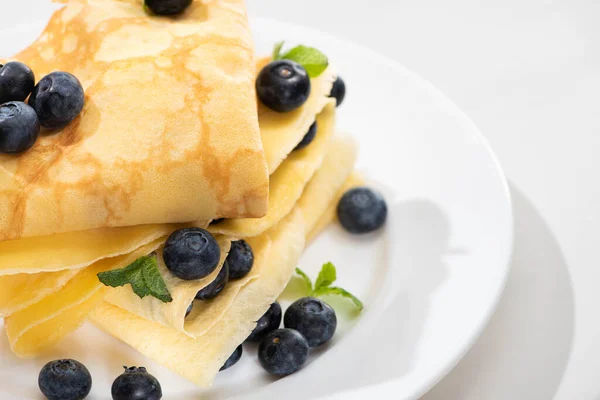 Vista de cerca de crepes sabrosos con menta y arándanos en el plato sobre fondo blanco - foto de stock