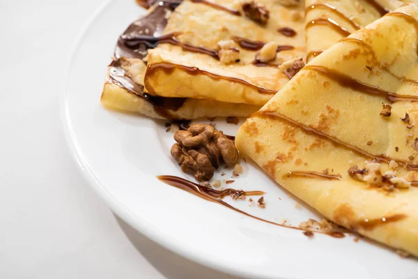 Close up view of tasty crepes with chocolate spread and walnuts on plate on white background — Stock Photo