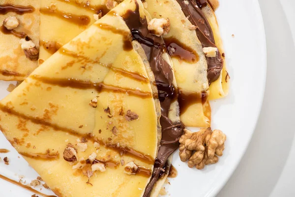 Close up view of tasty crepes with chocolate spread and walnuts on plate on white background — Stock Photo