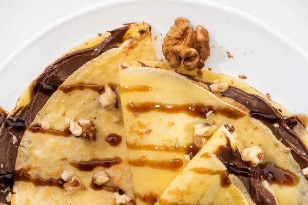 Top view of tasty crepes with chocolate spread and walnuts on plate on white background — Stock Photo